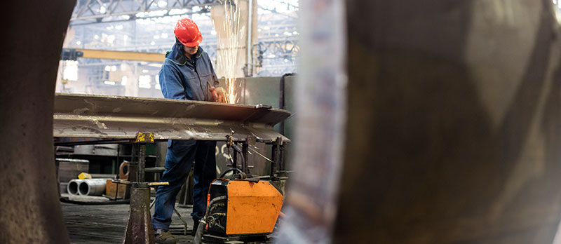 welding_guy Man with hardhat welding in background, large metal container in foreground